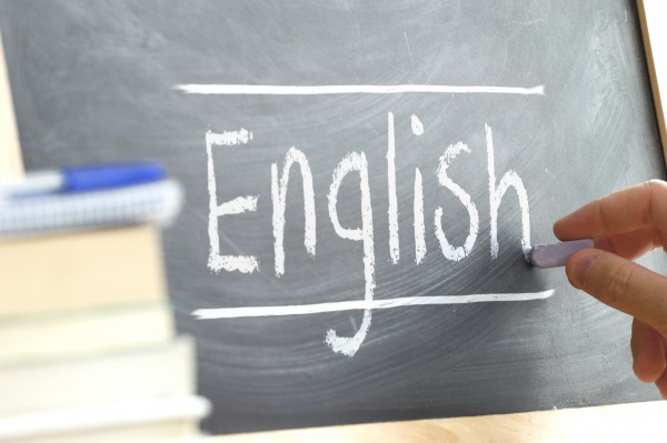 Hand writing on a blackboard in a language class with the word "English" wrote on. Some books and school materials.